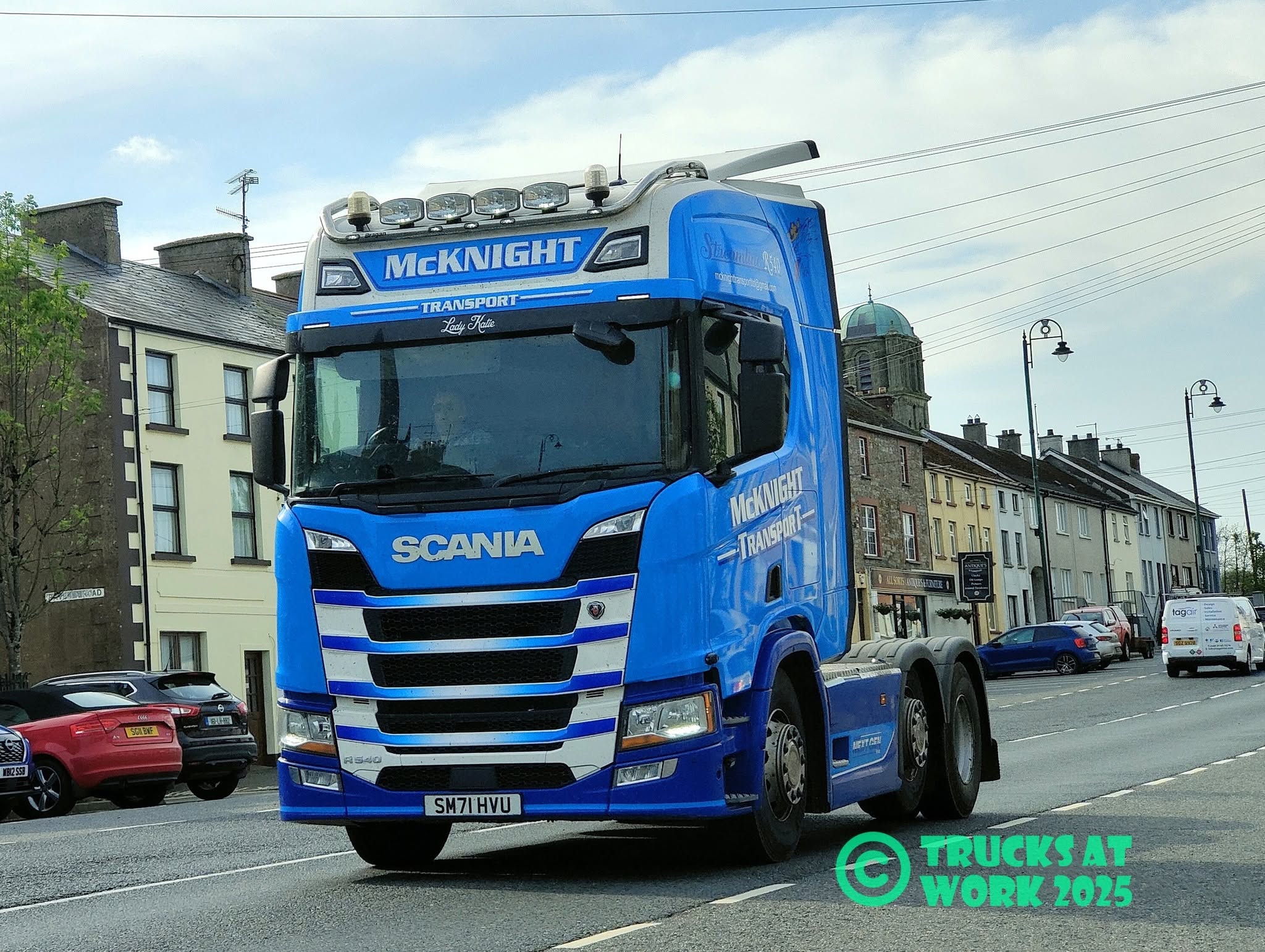 Blue McKnight Scania R540 tractor unit on the road, with the Trucks at Work 2025 photographer credit visible